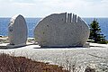 Foto scattata lungo la costa con l'oceano sullo sfondo.  In primo piano ci sono due pietre semicircolari, una vista di profilo a sinistra, l'altra di spalle al centro.