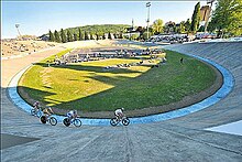 Fotografia de um velódromo ao ar livre com quatro corredores na pista.