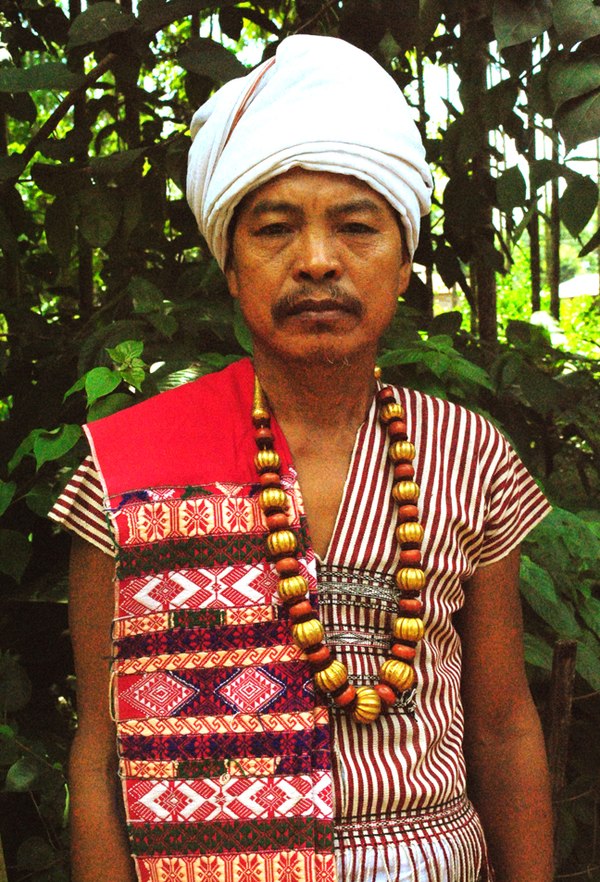 A Karbi elder in traditional attire, wearing a Poho (white turban), a choi-hongthor (woven jacket), a lek paikom (gold-plated necklace) and another po