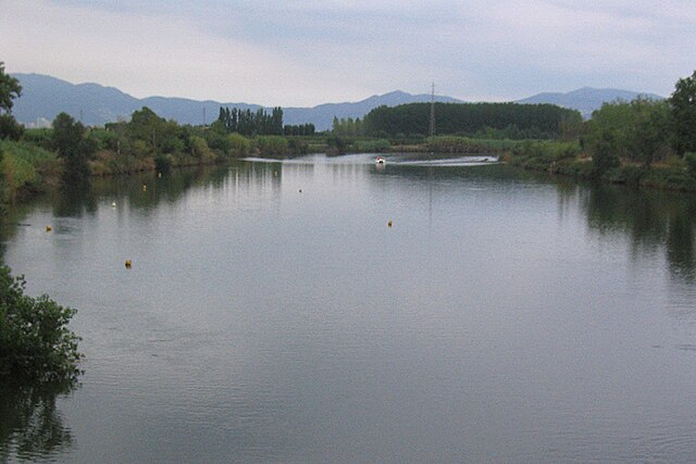 A wide, dark river in cloudy weather. In the background there are distant mountains, covered in mist.