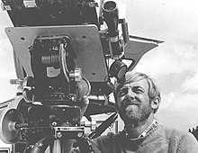 Fotografía en blanco y negro;  un hombre entrecierra los ojos por el ocular telescópico de un gran dispositivo mecánico