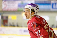 Foto van een hockeyspeler, kofferbak, in profiel, gekleed in een rode trui, naar links kijkend