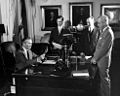 Forrestal is shown seated at his desk surrounded by staff while Secretary of Defense.
