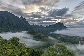 Montagnes karstiques, nuages colorés et brume au lever du jour, vue sud depuis le sommet du mont Nam Xay, durant la mousson, à Vang Vieng.