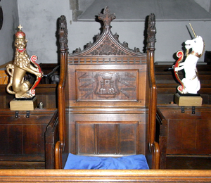 The Mayor's Pew, St Peter's Church, Barnstaple. On the chair back are shown the arms of Barnstaple: Gules a castle of three towers conjoined argent the centre tower larger than the others, between two scrolls inscribed in Latin: Domini Nomen and Firmum Castellum ("The Name of God (is) a Strong Castle") MayorsPew StPetersChurch Barnstaple Devon.PNG