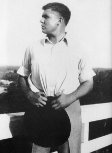 Black and white photograph of Robert E. Howard as a young man standing by a white fence and looking left into the distance.