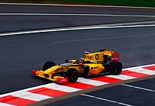 Žluté a černé vozidlo formule 1, které jelo na kopci na závodním okruhu