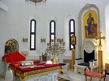 The Holy Place (sanctuary) in the church of the Saint Vladimir Skete at Valaam Monastery. To the left is the Holy Table (altar) with the Gospel Book, the tabernacle, and the seven-branch candlestand. The Table of Oblation is in the background to the left. To the right is the cathedra (bishop's throne). Saint Vladimir Skete (Valaam Monastery) 14.jpg