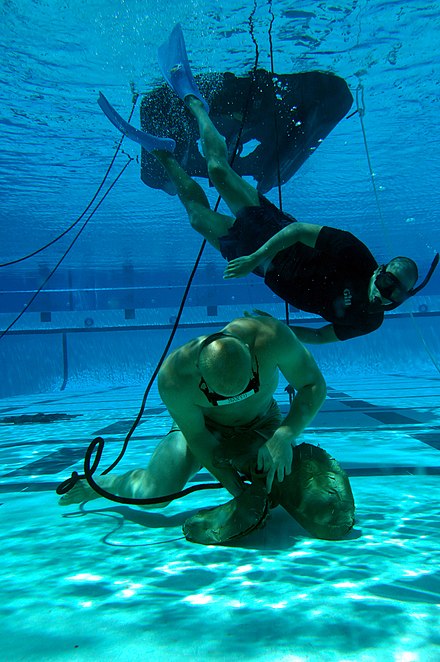 At BCT phase, a student demonstrates underwater knot tying skills during water proficiency testing while being roughed by instructors