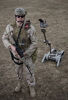 A U.S. Navy Sailor assigned to an explosive ordnance disposal team poses beside a PackBot. US Navy 090310-N-7090S-001 Explosive ordnance disposal technicians are using remote-controlled machines to help detect and defuse improvised explosive devices.jpg