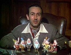 A color photograph of a man sitting behind a desk. Seven figurines are standing before him.