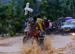 A bicycle rider carrying a passenger with crosses hustles his way through a flooded road in Kigali Photo by Emmanuelkwizera
