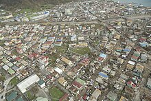 An aerial view of part of Roseau, revealing widespread damage to roofs. Flash floods clogged roads with debris--vegetative and structural--and mud. Aerial view of part of Roseau, the capital city of Dominica.jpg