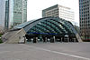 A wide, grey archway with a blue sign reading "CANARY WHARF STATION" in white letters and a man in a black suit walking through