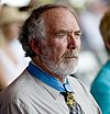 Perfil de um homem branco com uma barba farta e grisalha, usando uma medalha em forma de estrela de uma fita azul em volta do pescoço.