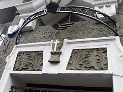 The doorways of the Corona Bar have images of a cross on the palm of a hand, supposedly the origin of the name of the village Entrance door head, Corona Bar, Crossmyloof.jpg