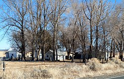 Photograph of the Eskelin Ranch, including a house and several agricultural buildings shaded by tall trees on a broad treeless plain