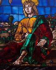 Detail of a stained glass window depicting a saint dressed in yellow, green and red robes, holding a quill.