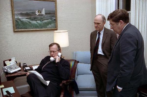 President George H. W. Bush sits at his desk in the Oval Office Study as Chief of Staff John Sununu stands nearby.