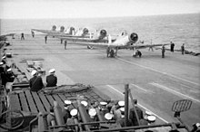 Photo en noir et blanc d'avions alignés sur le pont d'un porte-avions.
