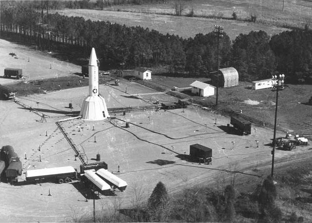 Jupiter missile emplacement showing ground support equipment. The bottom third of the missile is encased in a "flower petal shelter" of wedge-shaped m