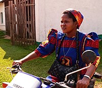 A sister of the Theresienne Sisters of Basankusu wearing a brightly coloured habit, riding a motor-bike, Democratic Republic of Congo, 2013[24]