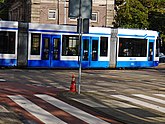 Photo of a tram, crossing the street in front of city gate; free photo Amsterdam, Fons Heijnsbroek, 10-2021