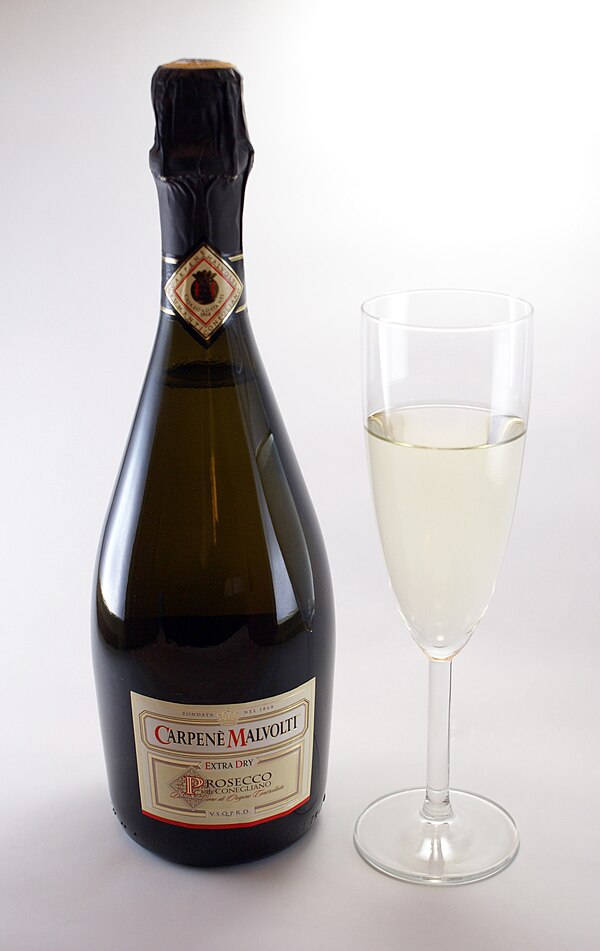 A bottle of Prosecco di Conegliano spumante extra dry and a glass of Prosecco frizzante, which stops forming bubbles soon after it is poured