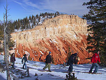 Una línea de raquetas de nieve con coloridos acantilados de roca en el fondo.