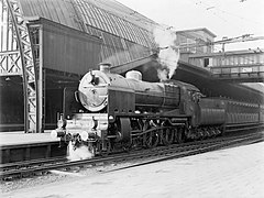 Un tren de pasajeros en el andén de la estación central, remolcado por una locomotora de vapor de la serie 3900