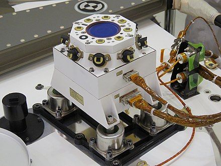 A la périphérie et sur le dessus de ce boitier fixé sur le pont de l'astromobile se trouvent 16 photodiodes mesurant la poussière présente dans l'atmosphère (capteur RDS). Au centre du boitier l'optique de la caméra SkyCam. Le tube noir à gauche du boitier est l'orifice du capteur de pression PS.