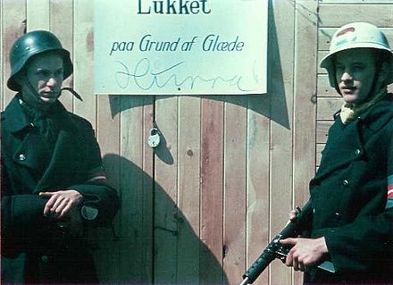 Closed due to happiness. Two Danish resistance fighters are guarding a shop while the owner is celebrating the liberation of Denmark on 5 May 1945. The man on the left is wearing a captured German Stahlhelm, the one on the right is holding a Sten gun.