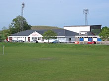 Fotbollsplan med låg, sluttande takbyggnad i bakgrunden