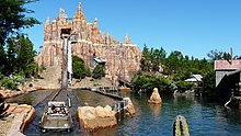The splashdown drop out of Wild West Falls' artificial mountain; a boat loaded with passengers in the foreground courses the channel back to the station.