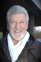 Photo d'un homme âgé, aux cheveux et à la barbe blanche, souriant.