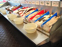 Self-serve display at a New England fish market. Customers use tongs to select their fish, then place it in a plastic tub for transfer to either the checkout counter or the fileting station. Self-serve display at a fish market.jpg