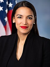 Alexandria Ocasio-Cortez tersenyum mengenakan jas hitam.