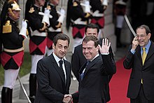 Two men shaking hands, one also waving