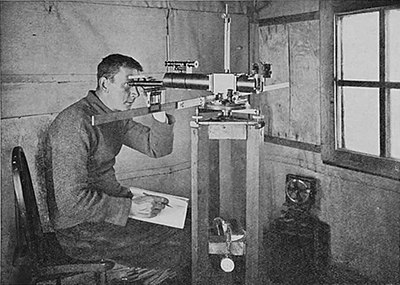 Photo of a man seated in a corner, looking into a complex tube with a wide crossbeam on a wooden brace