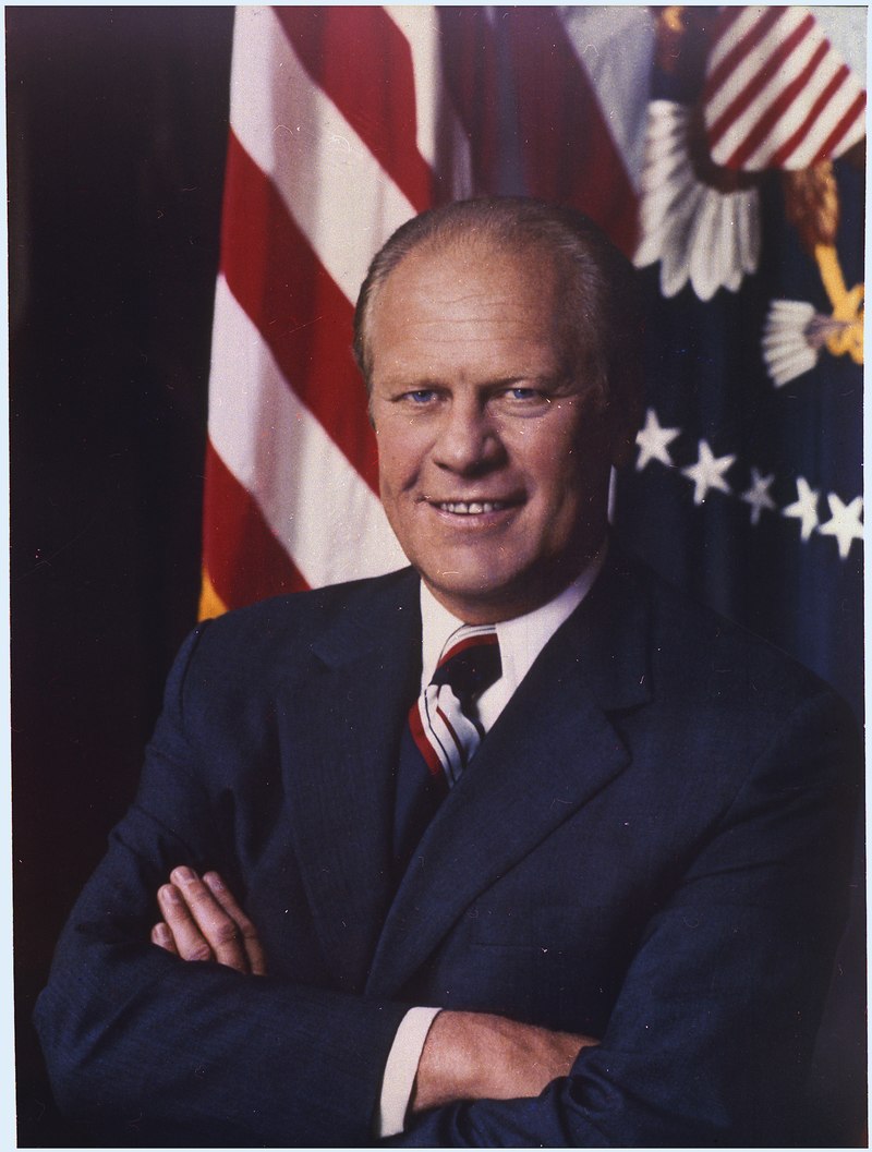 Ford, arms folded, in front of a United States flag and the Presidential seal.