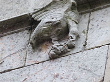 Fotografía en color de una escultura de dos animales en una fachada de piedra, bajo una cornisa sobresaliente.