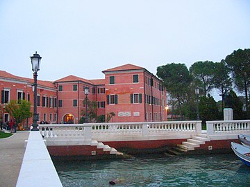 Photographie couleur d'un quai avec un double escalier descendant dans l'eau. En arrière-plan, un bâtiment de 2 étages à la façade rose.