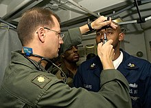 US Navy 040531-N-9630B-025 U.S. Navy Flight Surgeon, Lt. Cmdr. Scott Carlson of Downers Grove, Ill., performs and eye examination on Operation Specialist 1st Class Naron Williams of Jacksonville, Fla.jpg