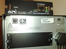 An AP9617 SmartSlot Network Management Card sitting on top of a Smart-UPS SMT1500I, showing the differences in slot keying APC AP9617 on top of SMT1500I.jpg