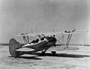 A two-seat biplane with 1930s U.S. insignia sits on an airport ramp.