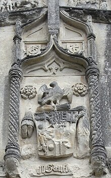 Arms of William Courtenay, 10th Earl of Devon (died 1511), of Tiverton Castle, above the south porch of St Peter's Church, Tiverton, next to the Castle. Part of the Greenway Chapel, built in 1517 by the wealthy Tiverton merchant John Greenway (died 1529), whose initials are seen above the Courtenay arms. Above and between two White Roses of York appears the heraldic badge of the Courtenays: A falcon rising holding in its claws a bundle of sticks, the Courtenay Faggot Courtenay Arms Tiverton Church Porch.JPG