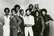 Earth, Wind, & Fire c. 1977. Front, from left: Verdine White, Al McKay, Philip Bailey, Maurice White, Andrew Woolfolk, Ralph Johnson. Back, from left: Larry Dunn, Fred White, Johnny Graham. Earth Wind and Fire 1970s press photo.jpg