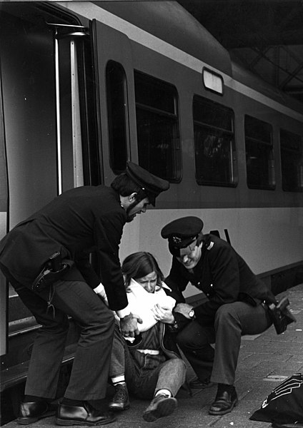 File:HUA-153325-Afbeelding van twee behulpzame beambten van de spoorwegpolitie bij een uit de trein gevallen vrouw.jpg