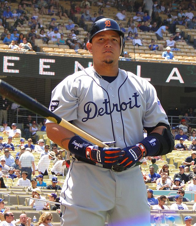 Un joueur de baseball en tenue portant des gants tient une batte dans ses mains.