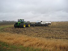 A large, modern John Deere model 9400 four-wheel drive tractor with tripled wheels and a drawbar-towed tool chain, including one-pass tillage equipment, planter and fertilizer applicator with tanks Modern John Deere Tractor IMG 0401.JPG